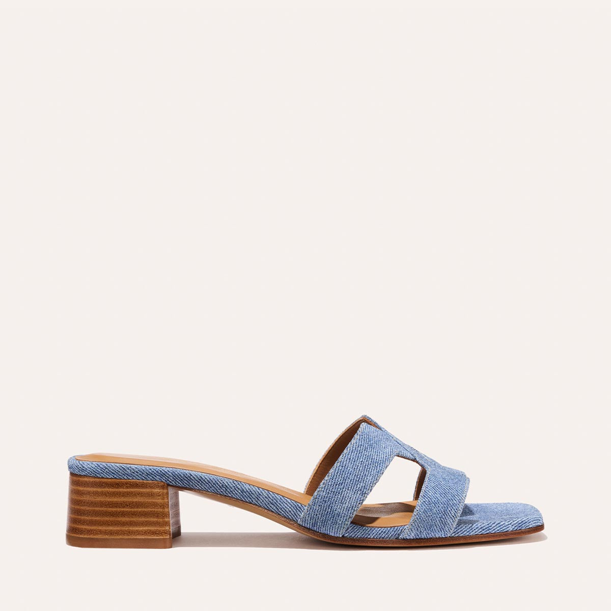 The MX 35 - Denim Suede by Margaux-development is a women’s open-toe slide featuring a blue denim upper, brown low block heel, and geometric side cut-outs, displayed against a plain light background.