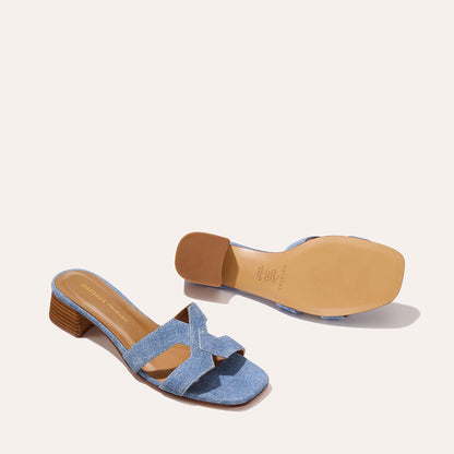 A pair of Margaux-development The MX 35 - Denim Suede women’s open-toe sandals featuring light blue crisscross straps, a walkable low brown block heel, and a tan sole. One sandal is upright; the other displays the bottom.