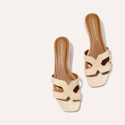 A pair of The MX 35 - Latte Calf sandals by Margaux, featuring beige crisscross straps, brown insoles, and a walkable block heel, displayed on a light background.