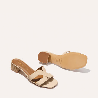 A pair of Margaux’s The MX 35 - Latte Calf sandals: one flat to display beige crisscross straps, the other on its side showing the walkable low block heel and sole.