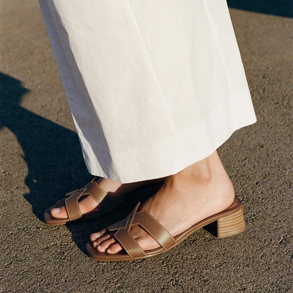 A person in white wide-leg pants and Margaux’s The MX 35 - Mocha Calf block heels stands on a sunlit pavement.