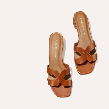The MX 35 - Saddle Calf by Margaux-development: brown leather slides with crisscross straps, square toes, and a subtle 1.5-inch heel, shown on a light background with brand name visible on the insole.