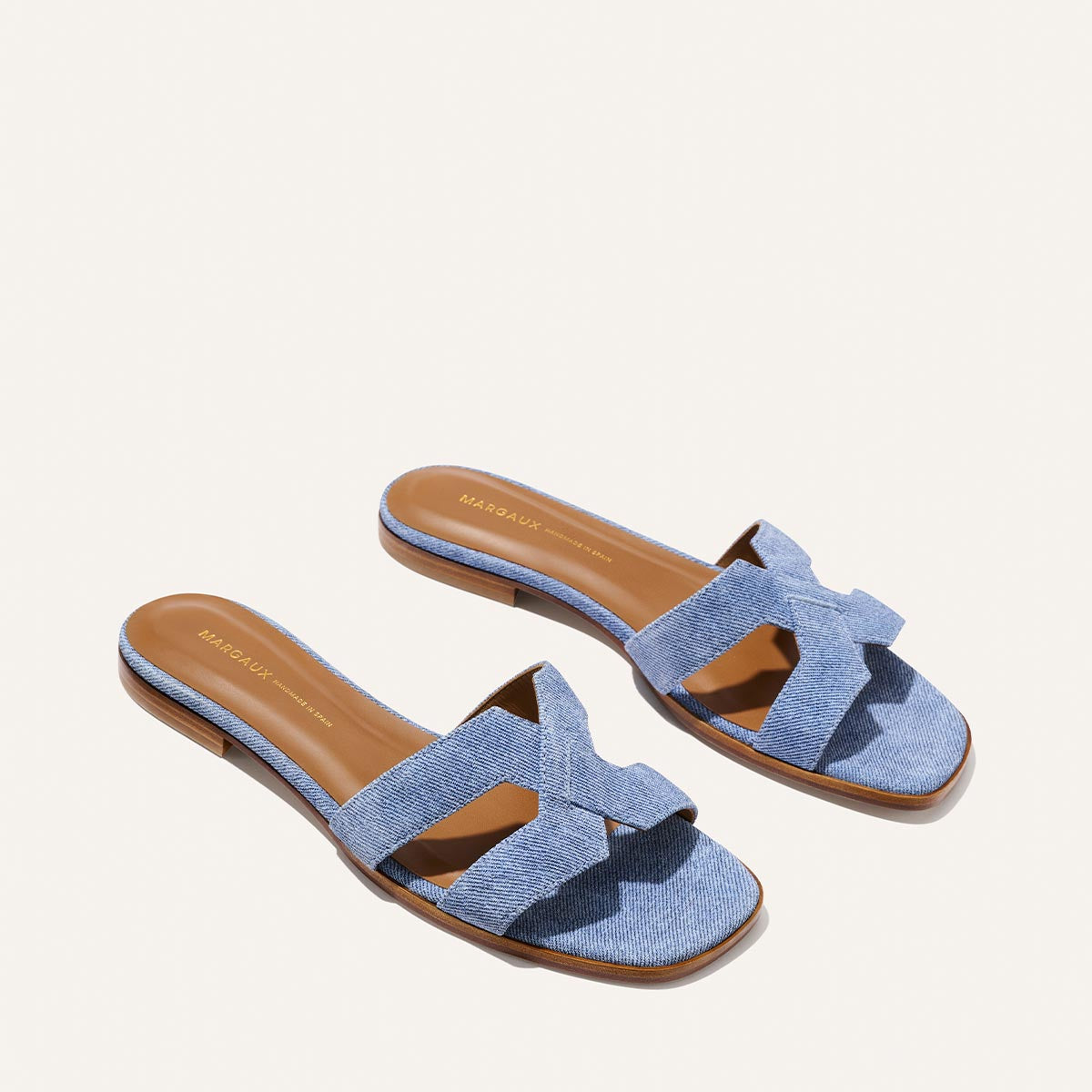 The MX Sandal - Denim Suede by Margaux features light blue crisscross suede straps and tan insoles, shown on a plain light background.