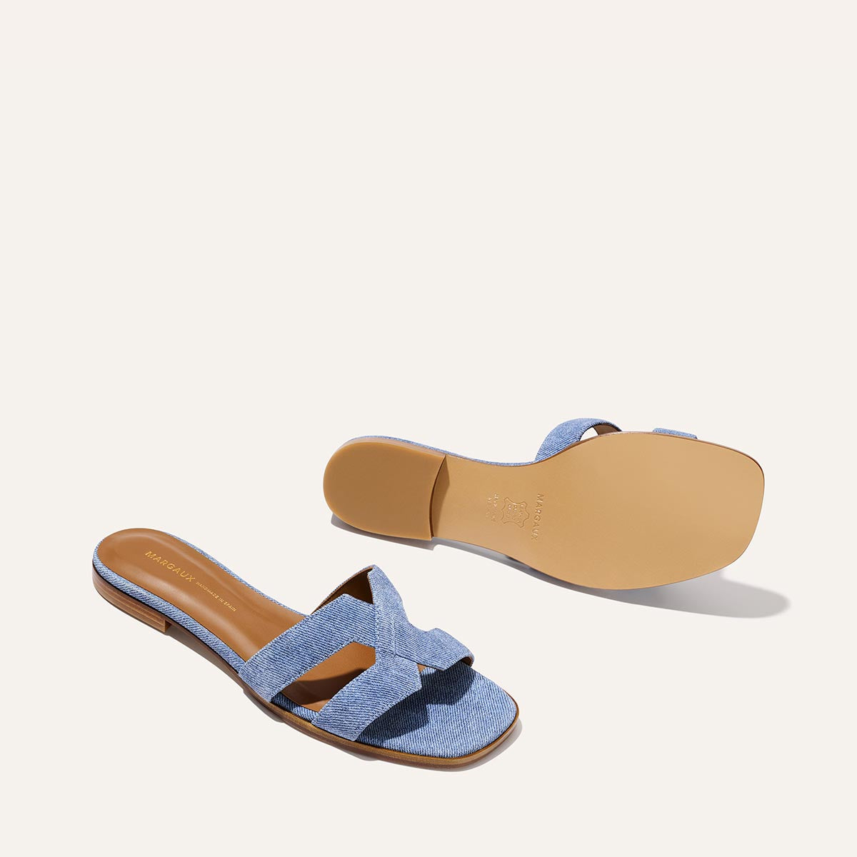 The MX Sandal - Denim Suede by Margaux features light blue crisscross straps and tan soles, displayed from the top and bottom on a plain, off-white background.