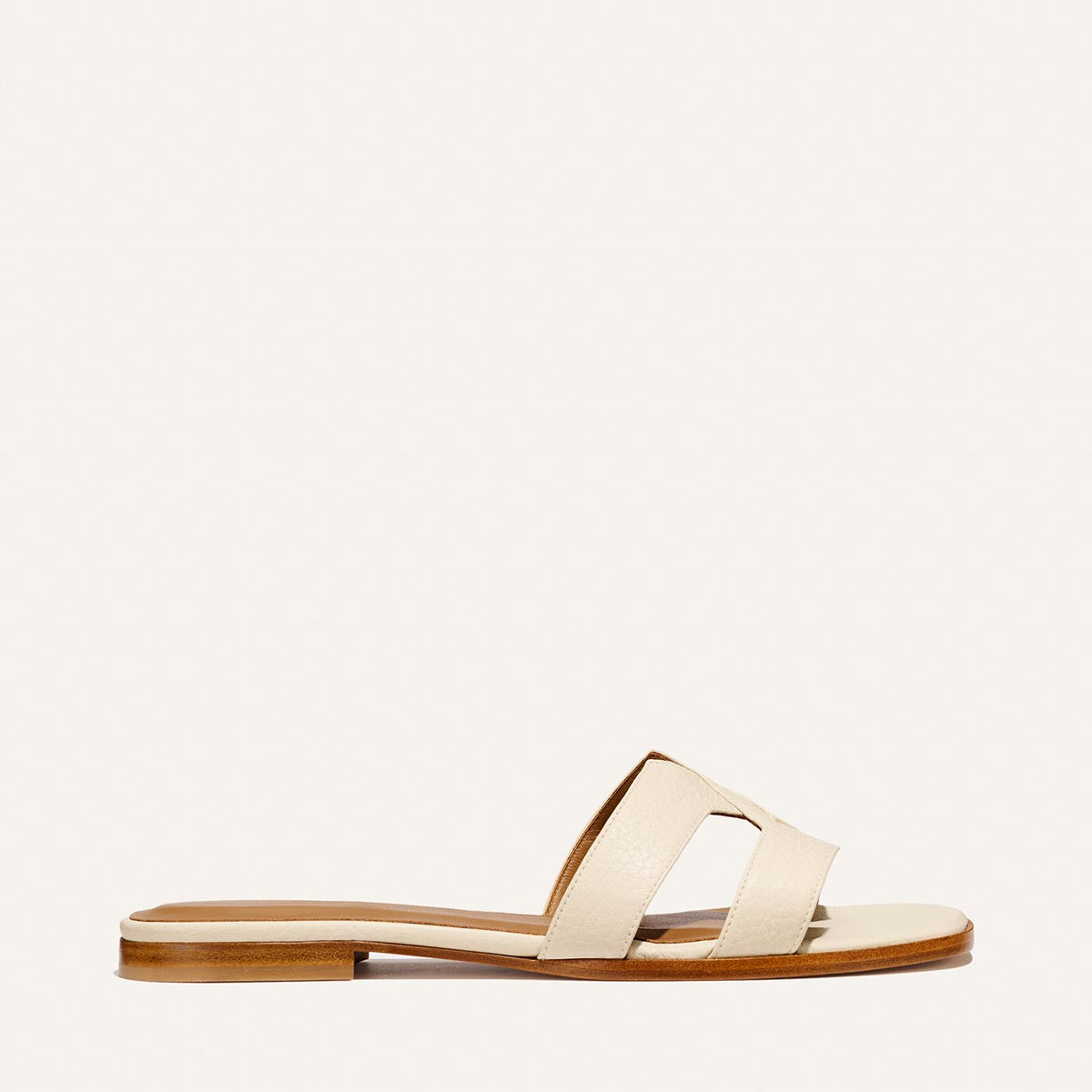 The Margaux MX Sandal in Ecru Tumbled Nappa features two wide luxe leather straps and a low wooden sole—a minimalist essential for effortless everyday style. Shown in side profile on a plain light background.