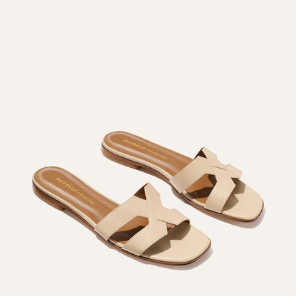 The MX Sandal - Latte Calf by Margaux: beige leather flats with crisscross straps, open toes, and a low wooden heel—your go-to sandal for elevated everyday style, shown on a light background.