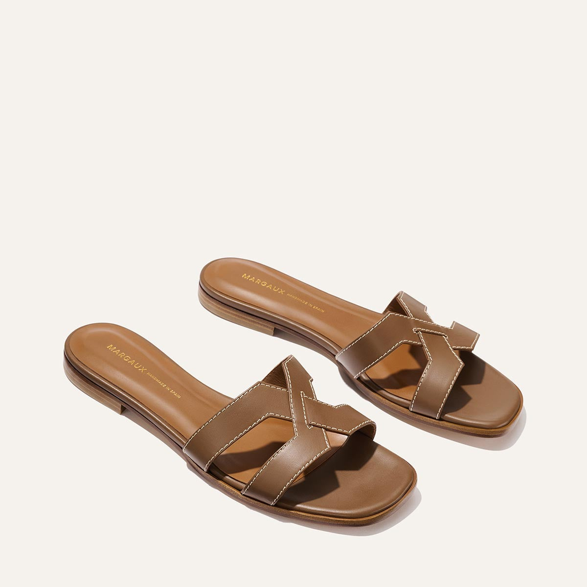 The MX Sandal - Mocha Calf by Margaux features brown open-toe slide sandals with crossed leather straps and white stitching, shown on a light background.