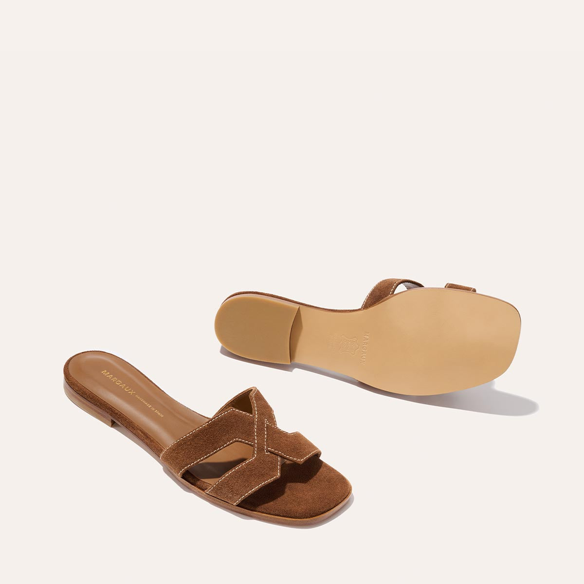 The MX Sandal - Saddle Suede by Margaux features brown suede crisscross straps and expert craftsmanship, with one sandal shown top-down and the other highlighting its smooth sole.