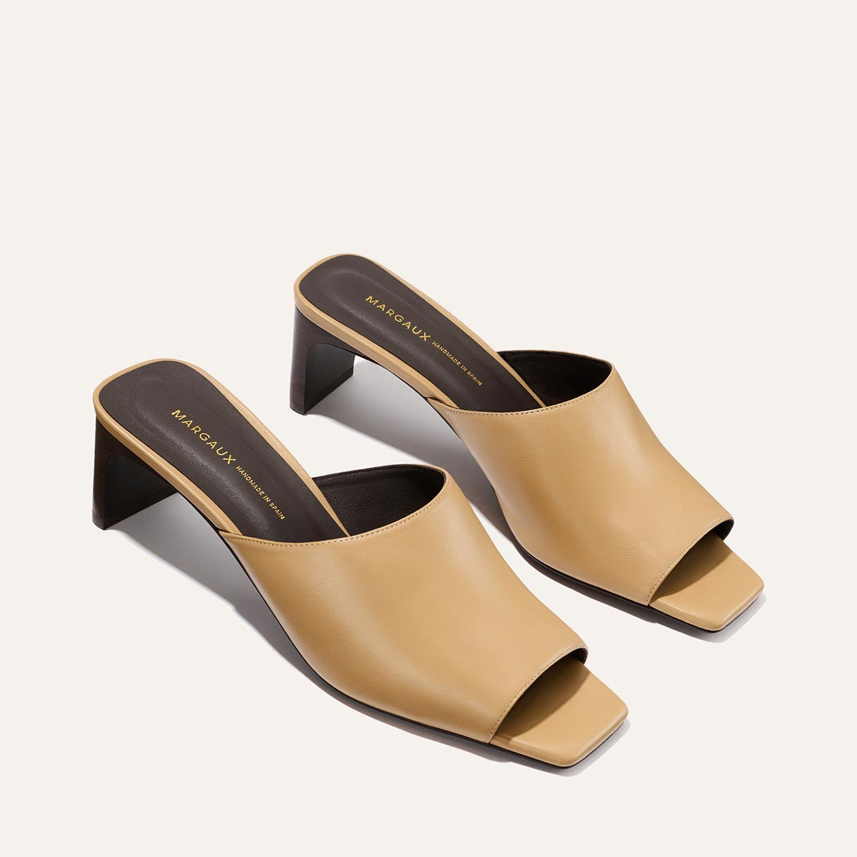 Pair of tan high-heeled mules on a light gray background
