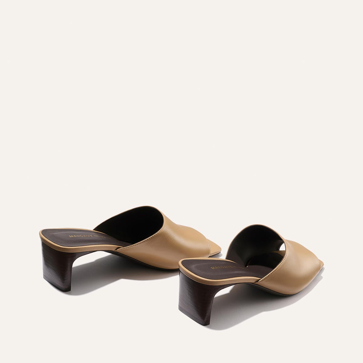Pair of tan and black high-heeled mules on a white background