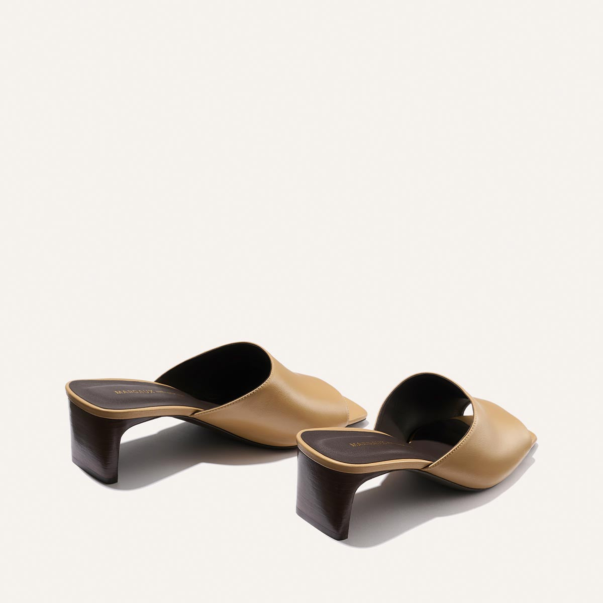 Pair of tan and black high-heeled mules on a white background