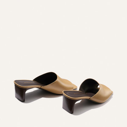 Pair of tan and black high-heeled mules on a white background