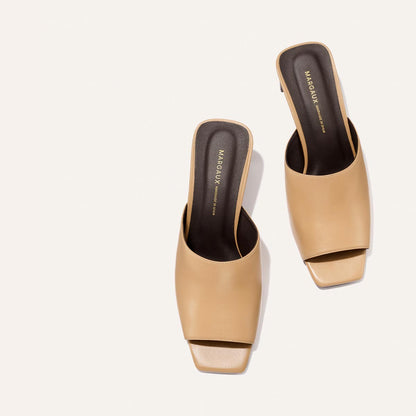 Pair of beige high-heeled mules on a light gray background