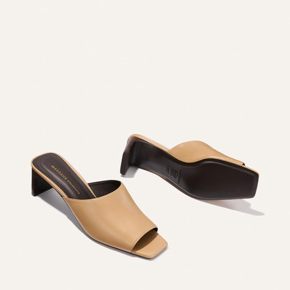 Pair of beige high-heeled mules with black soles on a light background