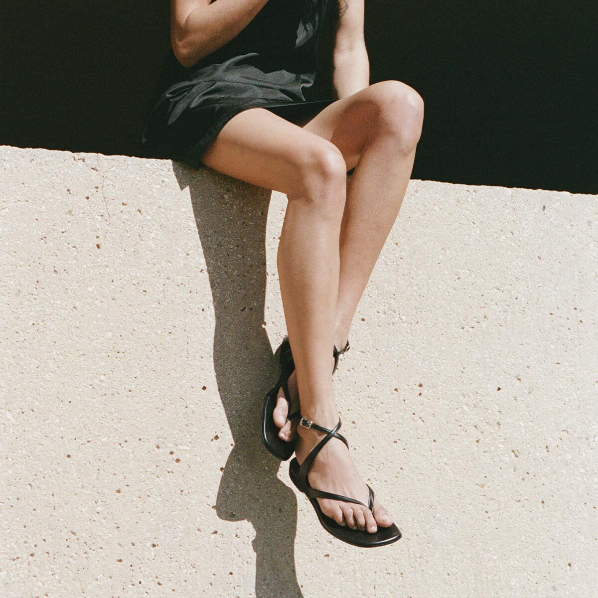 Person wearing black sandals sitting on a light-colored surface.