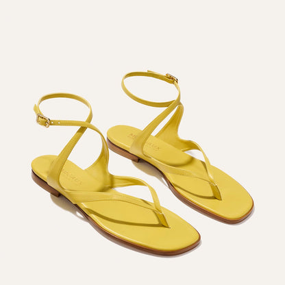 The Palermo Sandal - Chartreuse Nappa by Margaux features yellow leather, ankle straps, toe loops, flat brown soles, and gold buckles—a playful yet elevated look inspired by Julia Berolzheimer. Displayed on a light background.