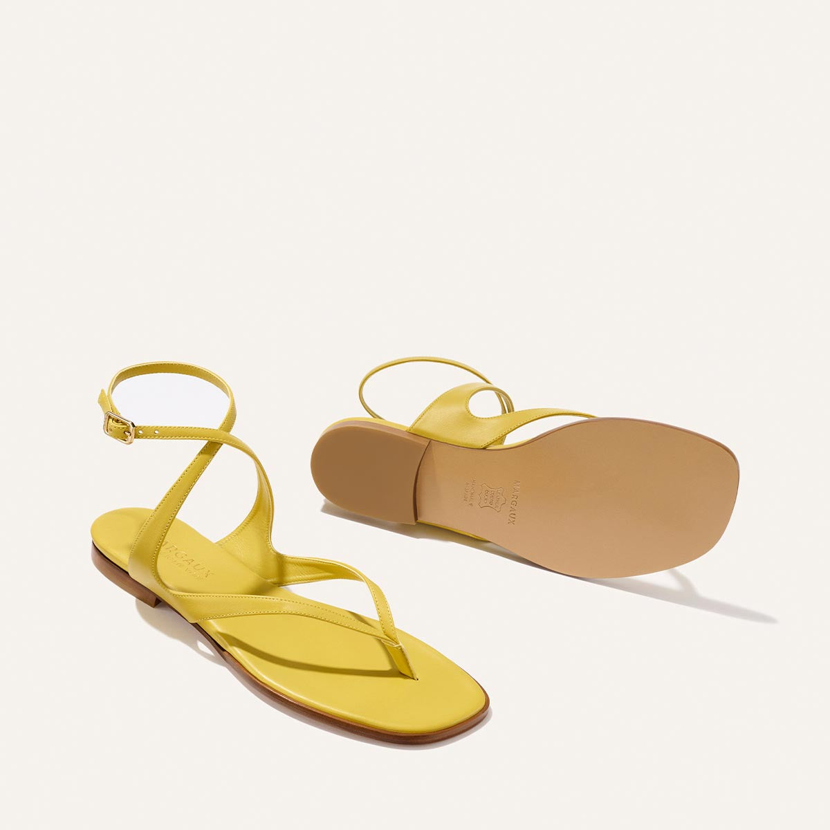 Margaux’s The Palermo Sandal in Chartreuse Nappa features yellow strappy flat sandals with ankle straps and toe loops—one upright, one showing the sole—on a light background, perfect for a playful twist to your elevated style.