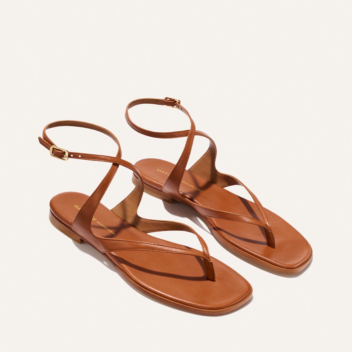 The Palermo Sandal - Saddle Nappa by Margaux features brown leather straps, ankle buckles, flat soles, and a minimalist design—ideal for summer days and shown against a light background.