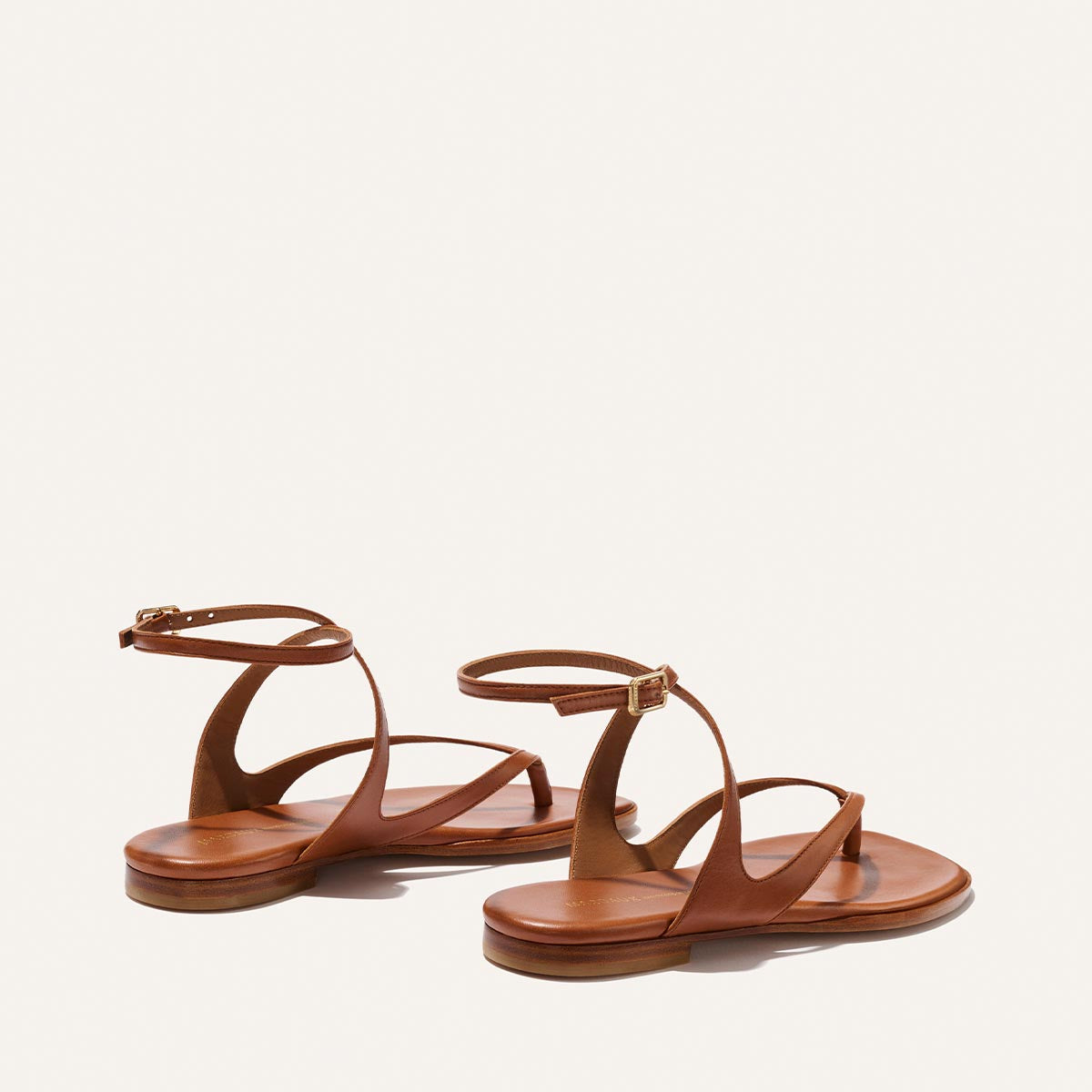 The Palermo Sandal - Saddle Nappa by Margaux: brown leather flat sandals with ankle and curved side straps, plus a cushioned insole—ideal for summer days. Shown against a plain off-white background.