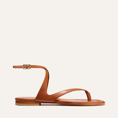 The Palermo Sandal - Saddle Nappa by Margaux is a brown leather flat with a minimalist design, featuring toe and curved upper straps, an ankle strap with buckle, and a cushioned insole for comfort—perfect for summer getaways.