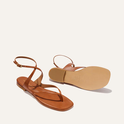 The Palermo Sandal - Saddle Nappa by Margaux: brown strappy flat sandals with ankle straps, buckle closures, and cushioned insoles. One sandal stands upright, the other shows the sole against an off-white background.