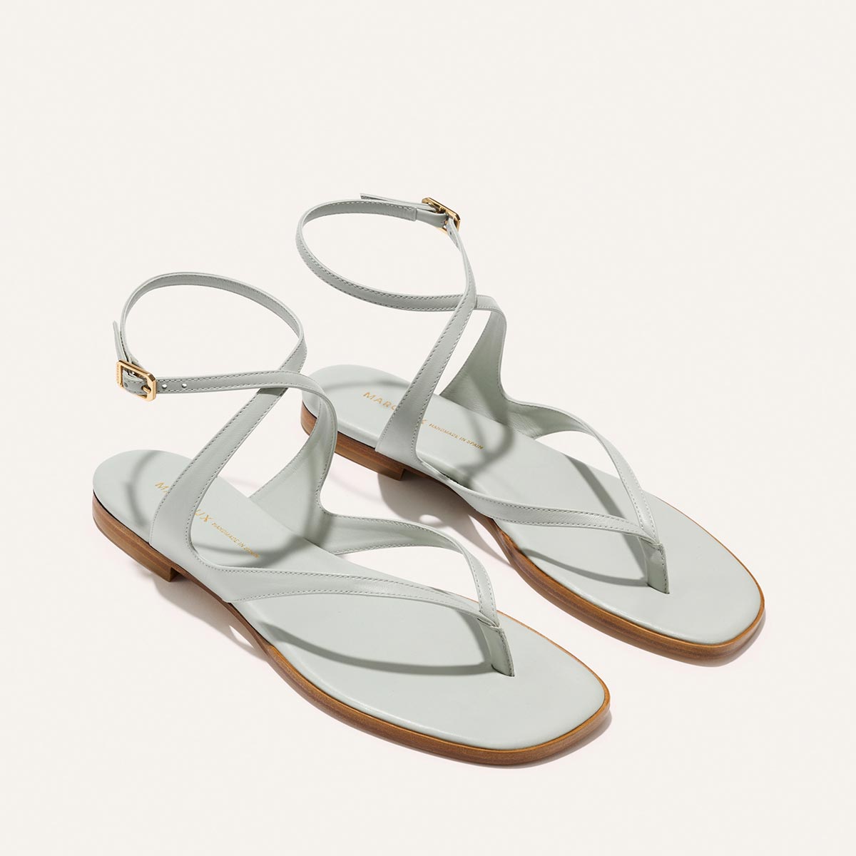 Sky Nappa Palermo sandals in light blue, featuring a flat thong design, an ankle strap with a gold buckle, and a cushioned insole.