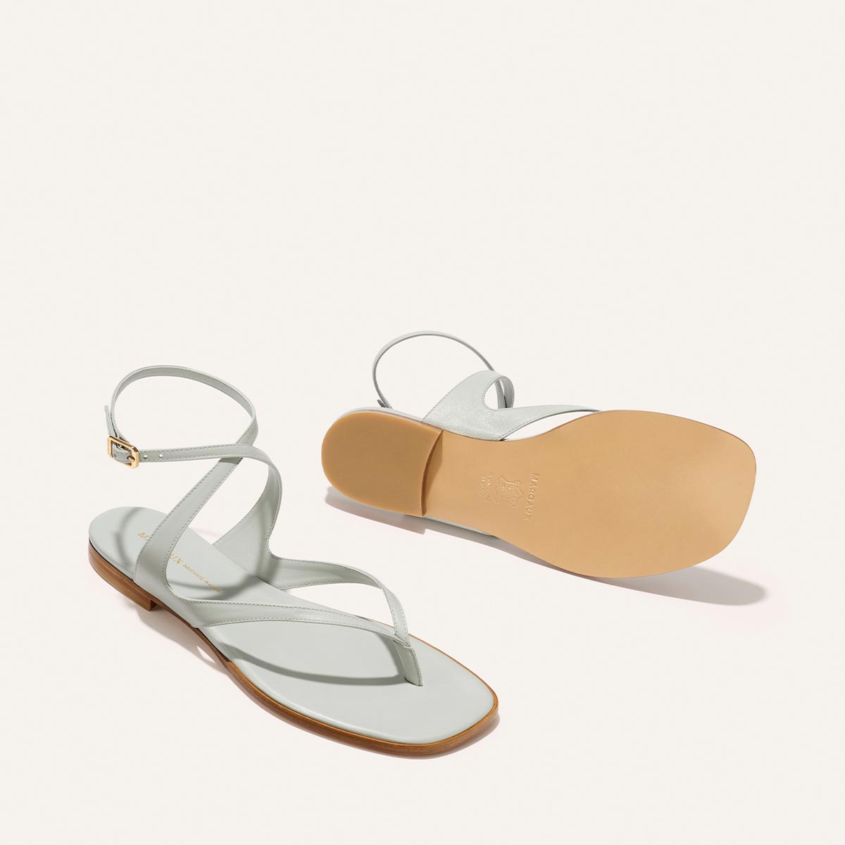 The Palermo Sandal - Sky Nappa in light blue with thin ankle straps and a thong-style toe, shown from the side and bottom, featuring a cushioned insole.