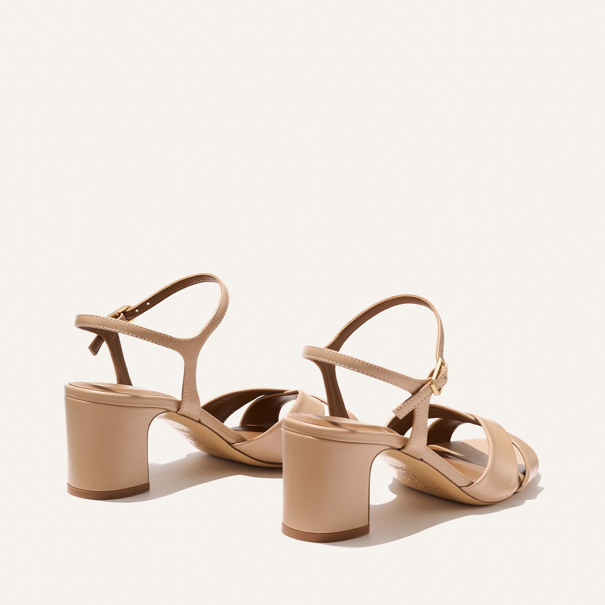 The Paloma Sandal - Dune Nappa by Margaux features beige open-toe heeled sandals with ankle straps and chunky block heels, shown from the back against a light background.