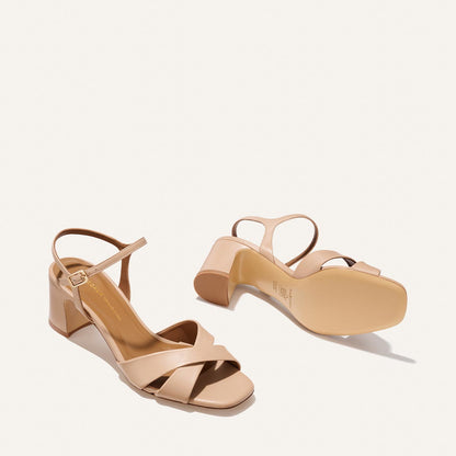 The Paloma Sandal - Dune Nappa by Margaux features beige block heels, open toes, crisscross front straps, and ankle straps with side buckles; one sandal is upright while the other rests on its side.