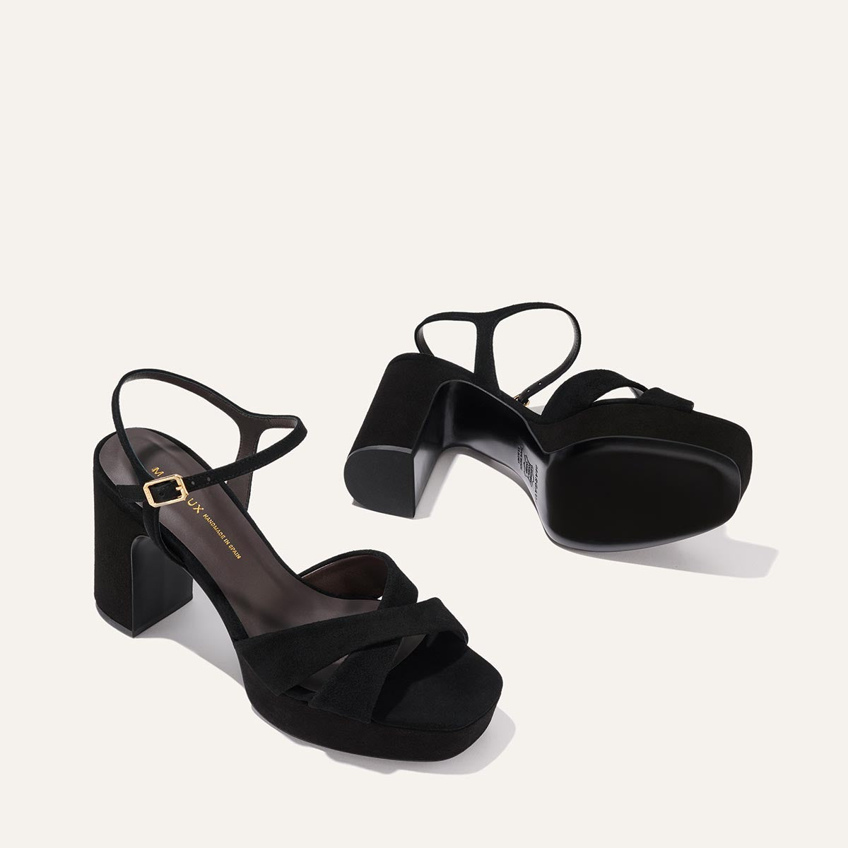 The Paloma Platform in Black Suede by Margaux features thick block heels, crisscross suede straps, gold-buckled ankle straps, open toes, and a padded platform for all-night comfort—perfect for any event.