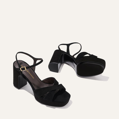 The Paloma Platform in Black Suede by Margaux features thick block heels, crisscross suede straps, gold-buckled ankle straps, open toes, and a padded platform for all-night comfort—perfect for any event.