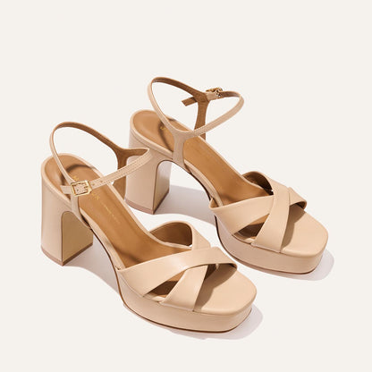 The Margaux Paloma Platform in Dune Nappa features beige chunky heels, crisscross straps, a cushioned platform for all-night comfort, ankle straps with buckles, and an open toe—all shown on a light background.