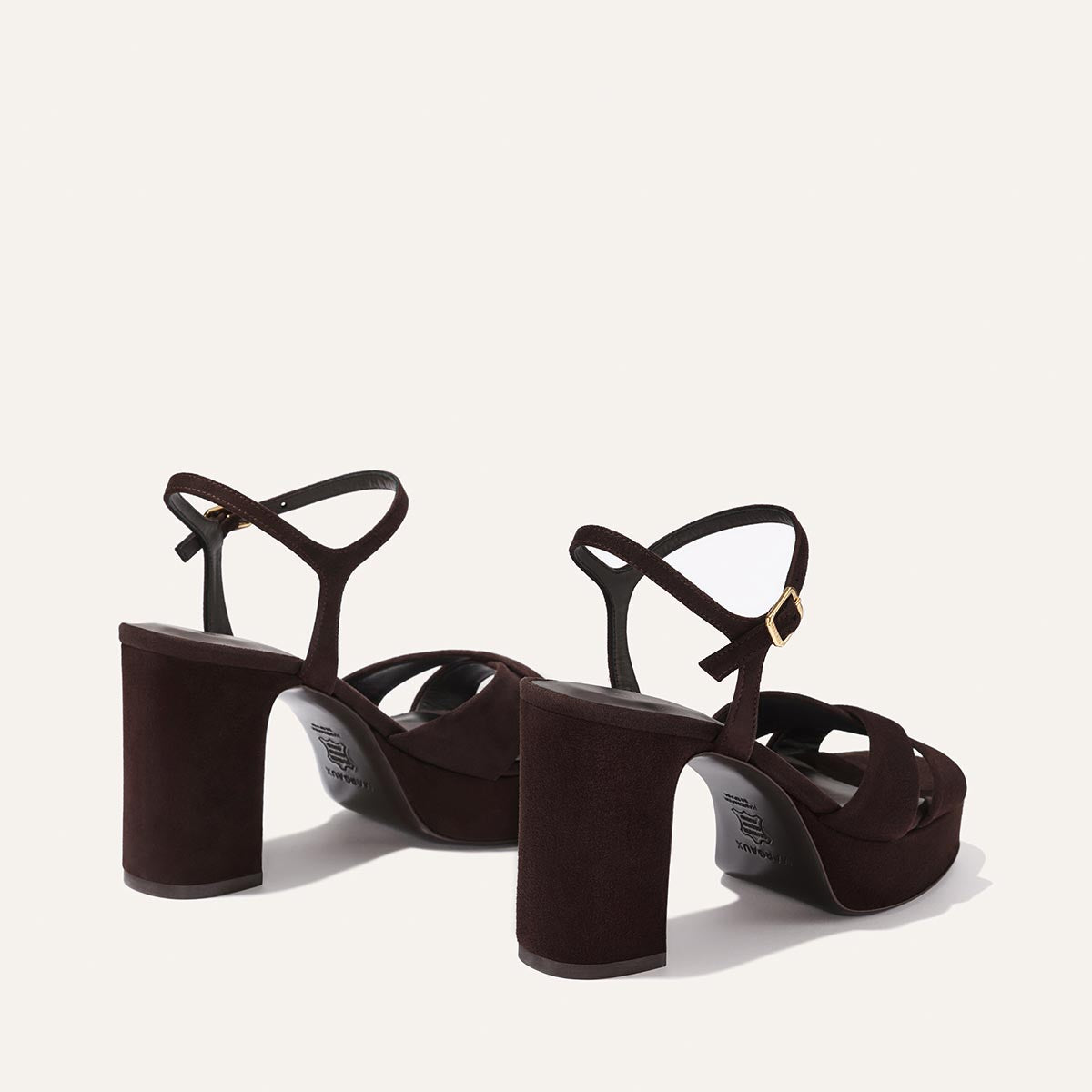 The Margaux Paloma Platform in Espresso Suede features chunky block heels, gold-buckled ankle straps, and a padded platform for comfort—all showcased on a light beige background.