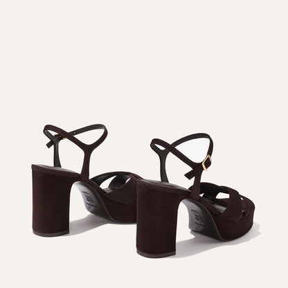 The Margaux Paloma Platform in Espresso Suede features chunky block heels, gold-buckled ankle straps, and a padded platform for comfort—all showcased on a light beige background.