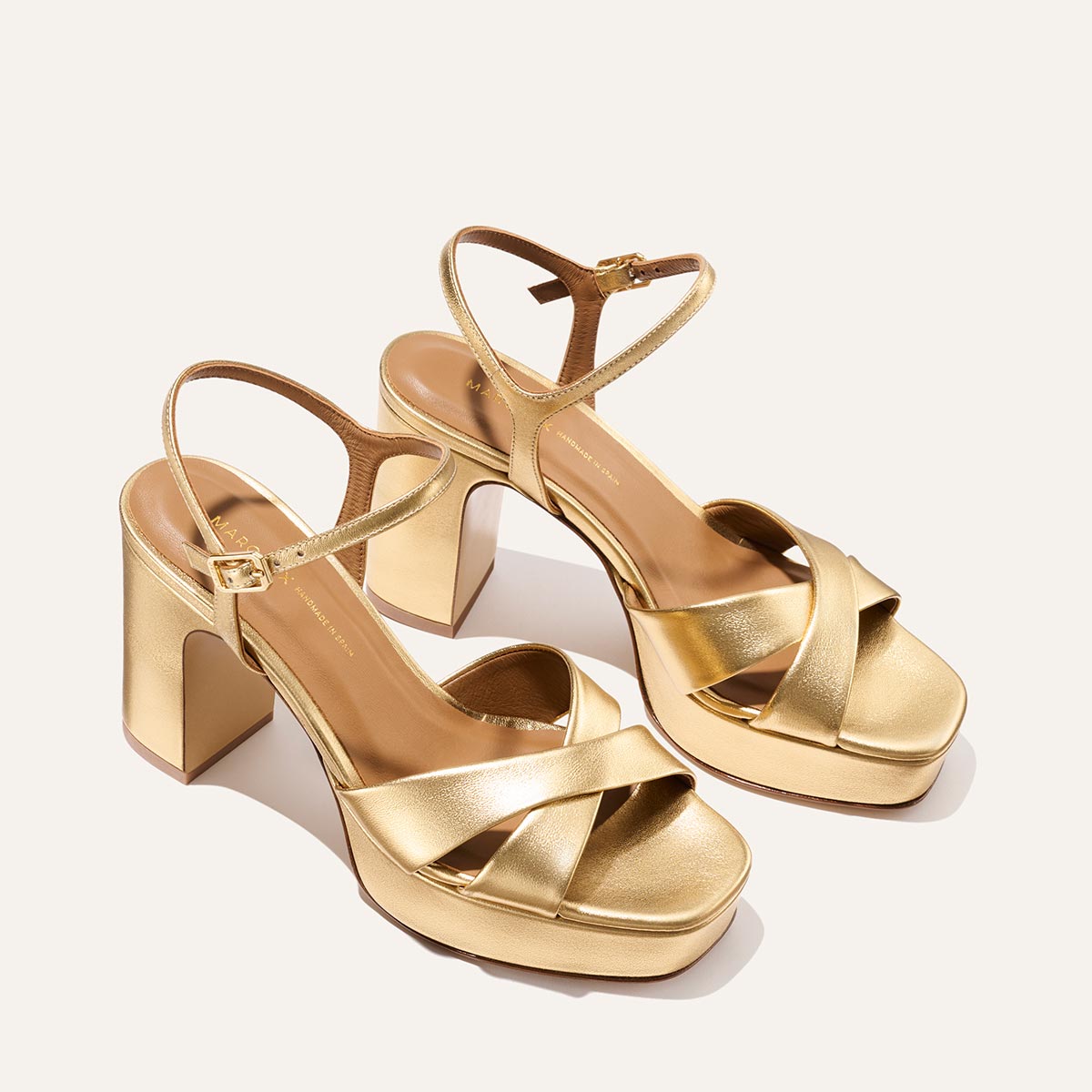 The Paloma Platform - Gold Nappa by Margaux features gold high-heeled platform sandals with padded soles, block heels, crisscross toe straps, and ankle buckles, shown on a neutral background.