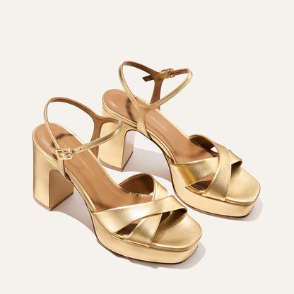 The Paloma Platform - Gold Nappa by Margaux features gold high-heeled platform sandals with padded soles, block heels, crisscross toe straps, and ankle buckles, shown on a neutral background.