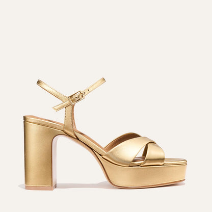 Step out in style with Margaux’s The Paloma Platform - Gold Nappa, showcasing a thick block heel, comfy crisscross toe straps, an adjustable ankle buckle, cushioned platform sole, and a shiny metallic gold finish.