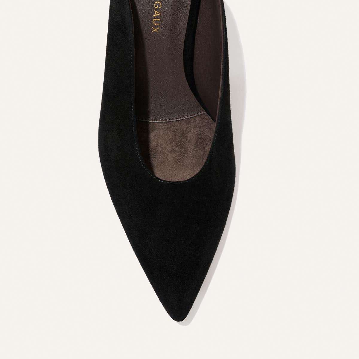 A top view of the Alison Roman x Margaux: The Parlor Mule in black suede by Margaux, highlighting the pointed-toe design and showcasing part of the insole and upper material against a light background.