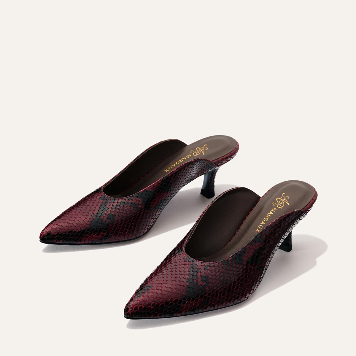 The Alison Roman x Margaux: The Parlor Mule in Burgundy Python Embossed by Margaux, featuring a pointed toe and black heel, is displayed on a light background.