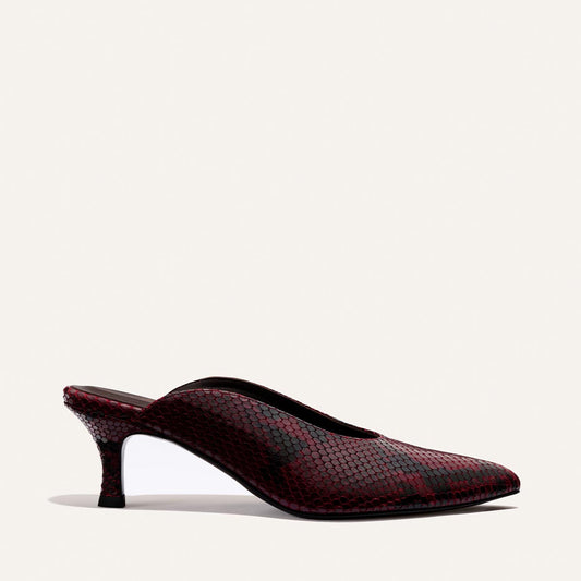 The Alison Roman x Margaux: The Parlor Mule in Burgundy Python Embossed by Margaux, featuring a red and black snakeskin pattern, pointed toe, and low heel, is shown against a plain white background.