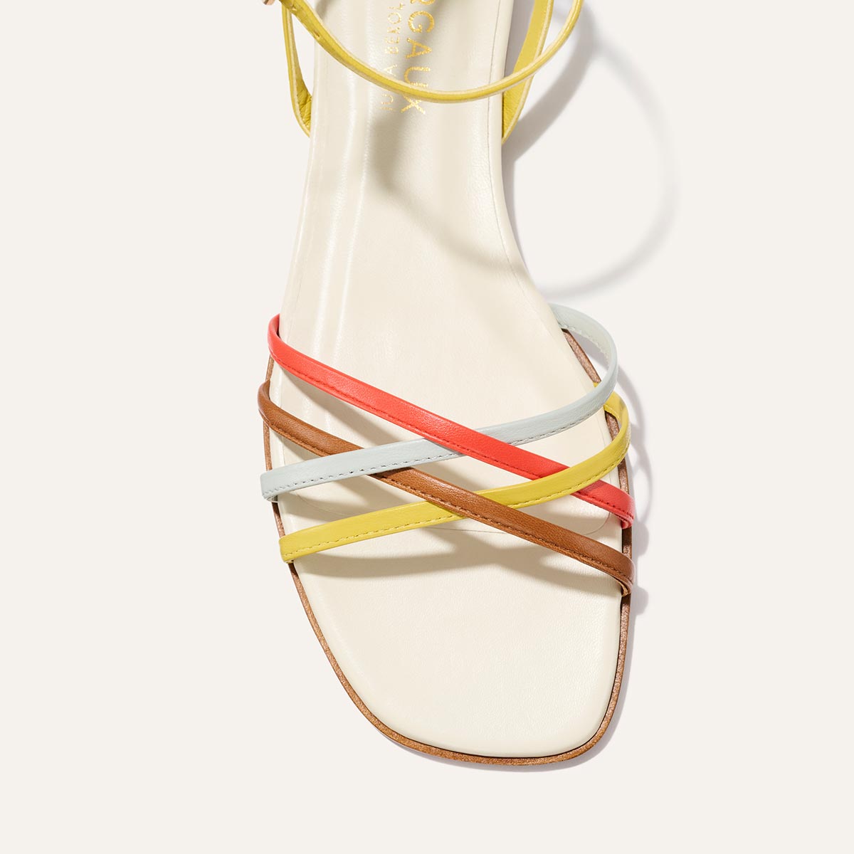 The Paros Sandal by Margaux features a square toe and thin, crisscrossing straps in cotton and multicolor nappa—yellow, white, coral, and brown—set on a cream-colored footbed for an elevated look.
