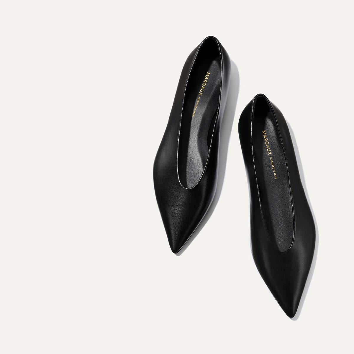 The Parra - Black Nappa flats by margaux-development feature a minimalist pointed-toe leather design with gold branding on the insoles, displayed against a light background.