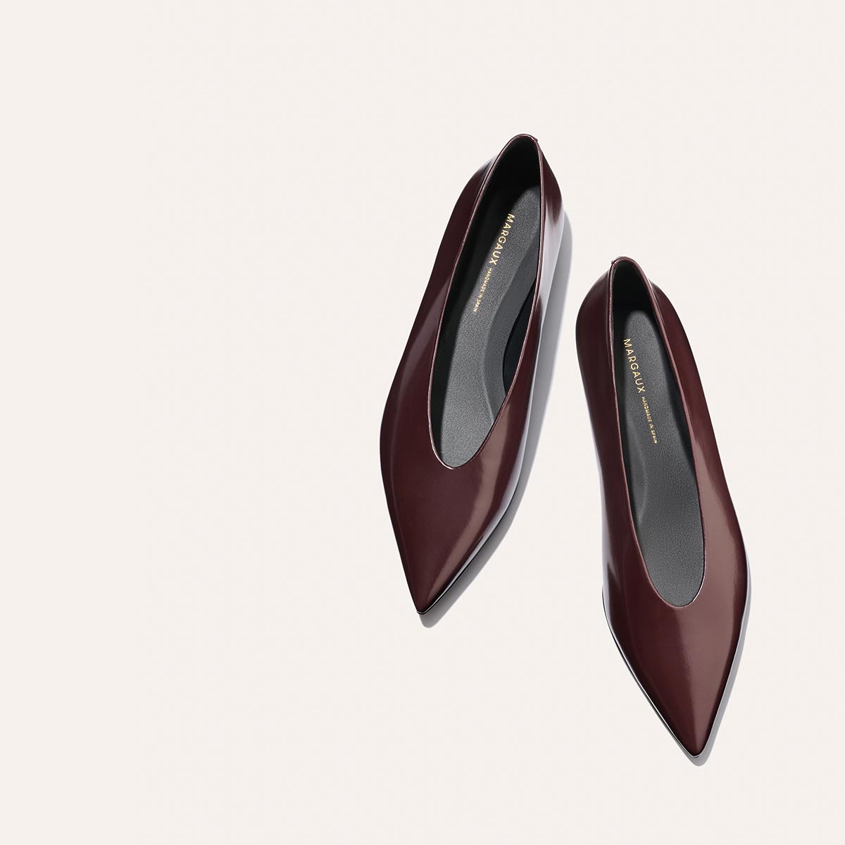 A pair of The Parra - Burgundy Calf pointed-toe shoes by margaux-development, featuring a glossy finish and high vamp, seen from above on a light off-white background.