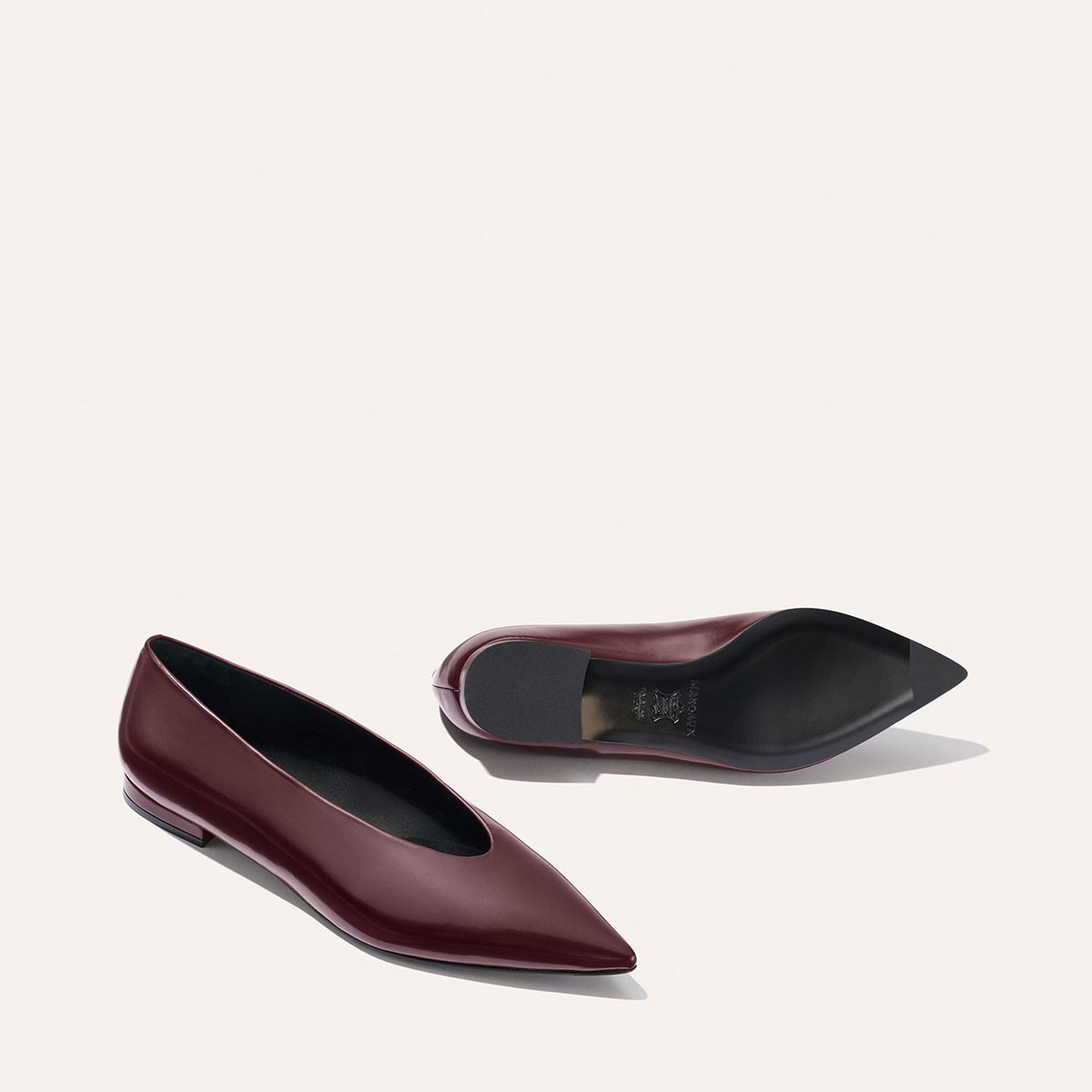 The Parra - Burgundy Calf flats by margaux-development are shown on a light background, with one shoe upright and the other on its side, highlighting the pointed toe, high vamp, structured silhouette, and sole.