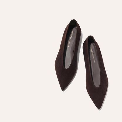The Parra - Espresso Suede flats by margaux-development are displayed on a light beige background, one shoe slightly angled toward the other, highlighting their dark brown pointed-toe suede design.