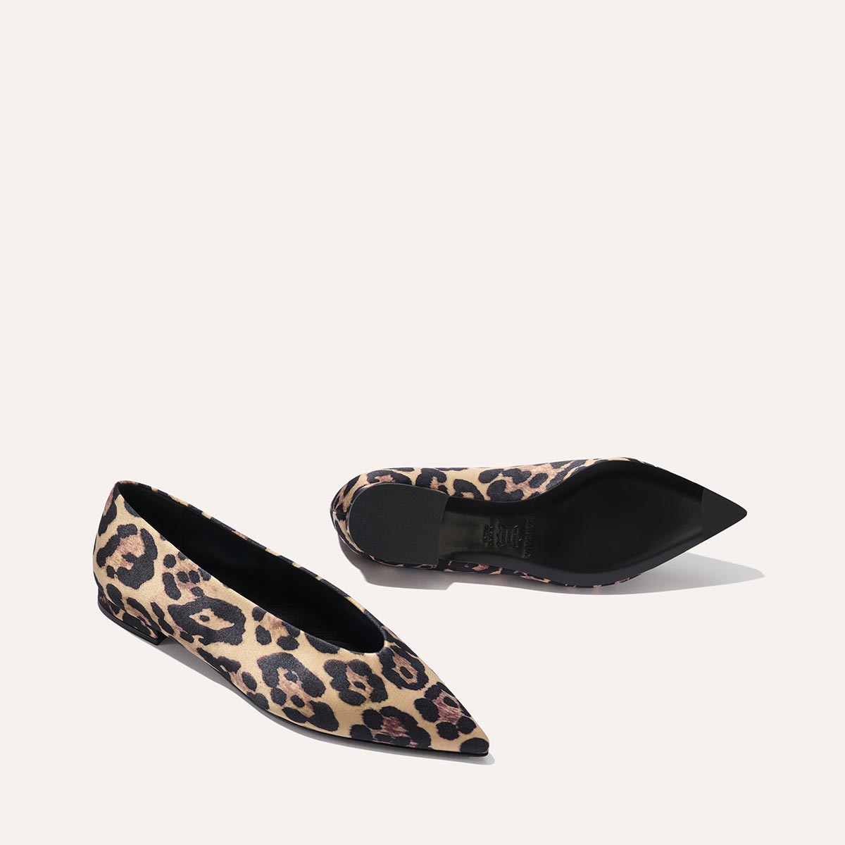 The Parra - Leopard Satin flats by margaux-development feature a pointed toe and tan and black leopard print, with one shoe upright and the other on its side against a plain light background.