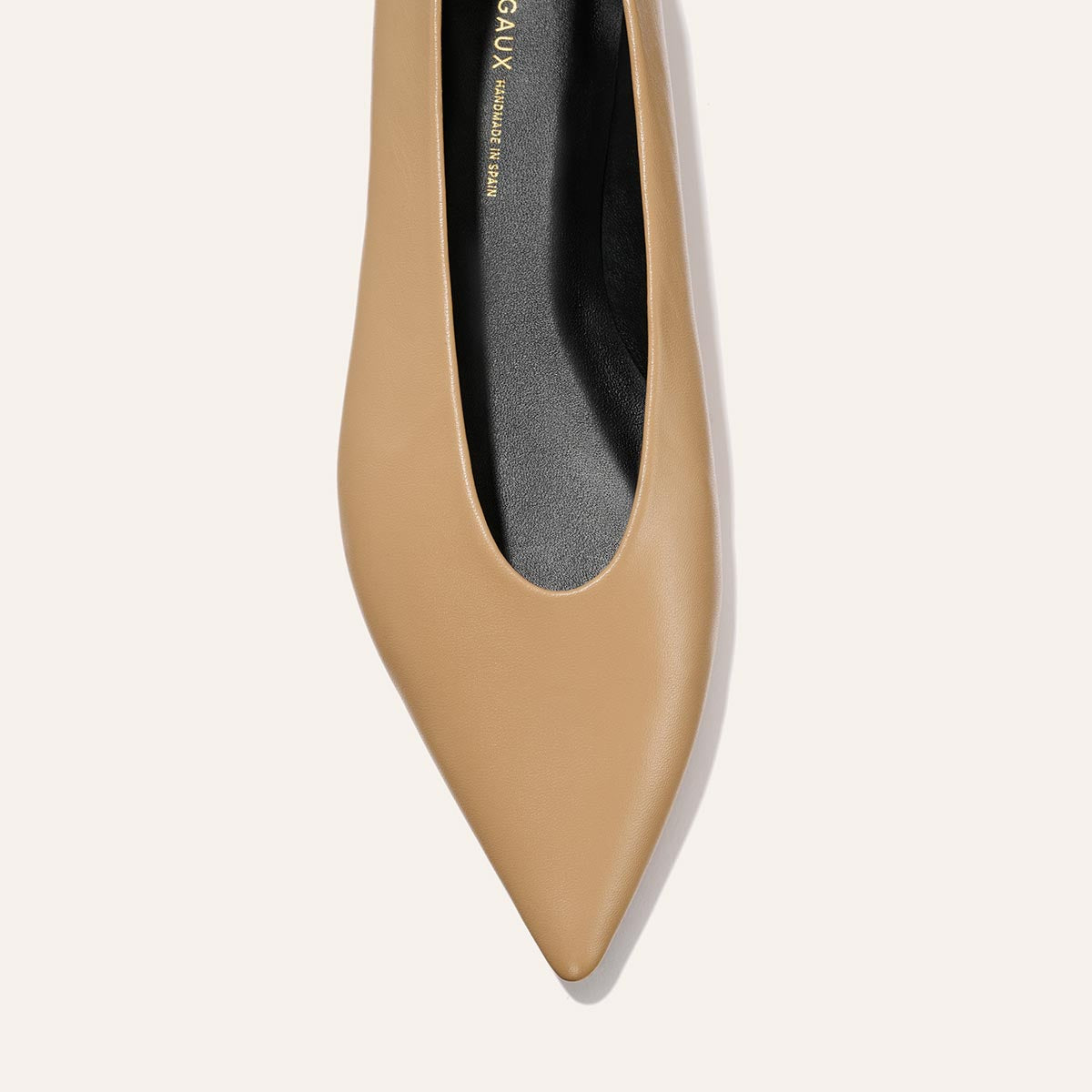 A top view of The Parra - Praline Nappa flat by margaux-development features a tan pointed toe, structured silhouette, and black insole against a light background.