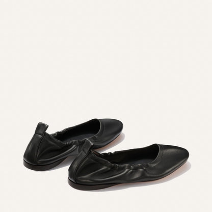 The Margaux Pascale - Black Nappa: a pair of black ballet flats with ruched detailing, rounded toes, and pull tabs at the heel, shown on a plain light background.
