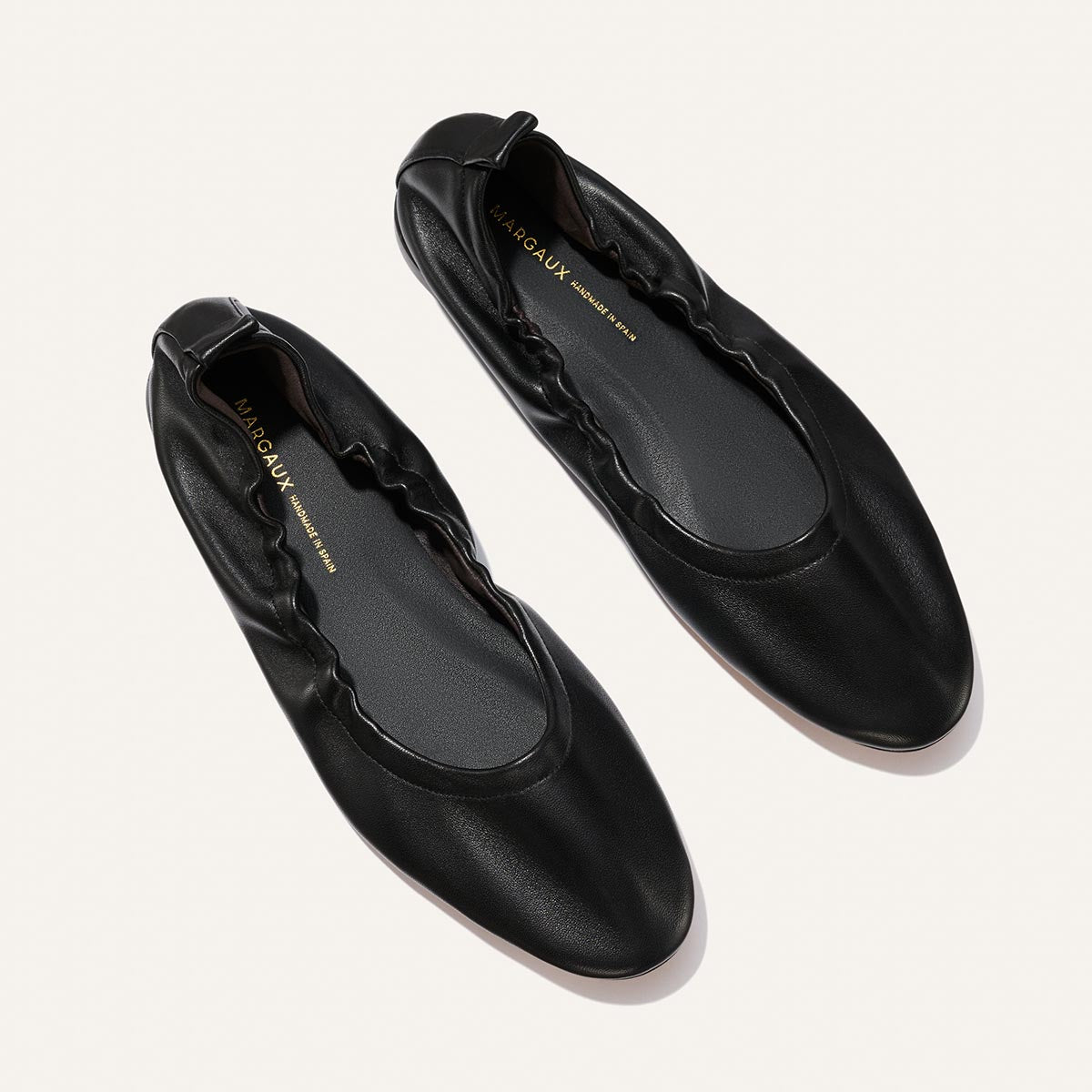The Pascale - Black Nappa by Margaux: black ballet flats with elasticized edges, a rounded toe, and Margaux branding on the insole, shown on a light background.