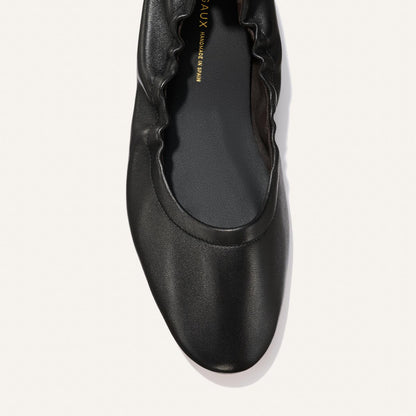 A top view of Margaux's The Pascale - Black Nappa flat shoe, featuring black leather with a ruched edge along the opening and a rounded toe, shown on a plain white background.